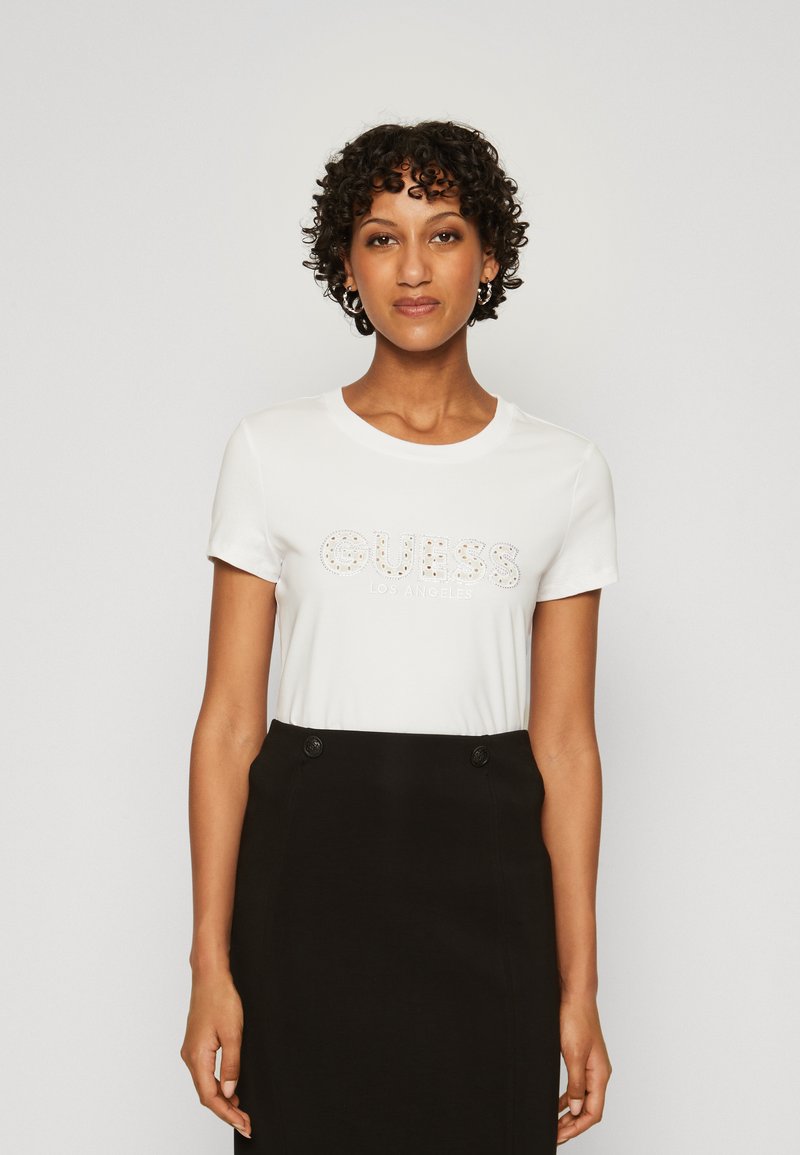 Camiseta blanca de manga corta con "GUESS LOS ANGELES" en strass. Combina con una falda negra de talle alto con detalles de botones.