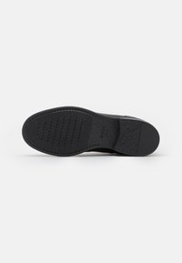 Suela de zapato negra con una superficie texturizada, que presenta ranuras y perforaciones para mayor tracción. Material de goma resistente, con tacón redondeado.