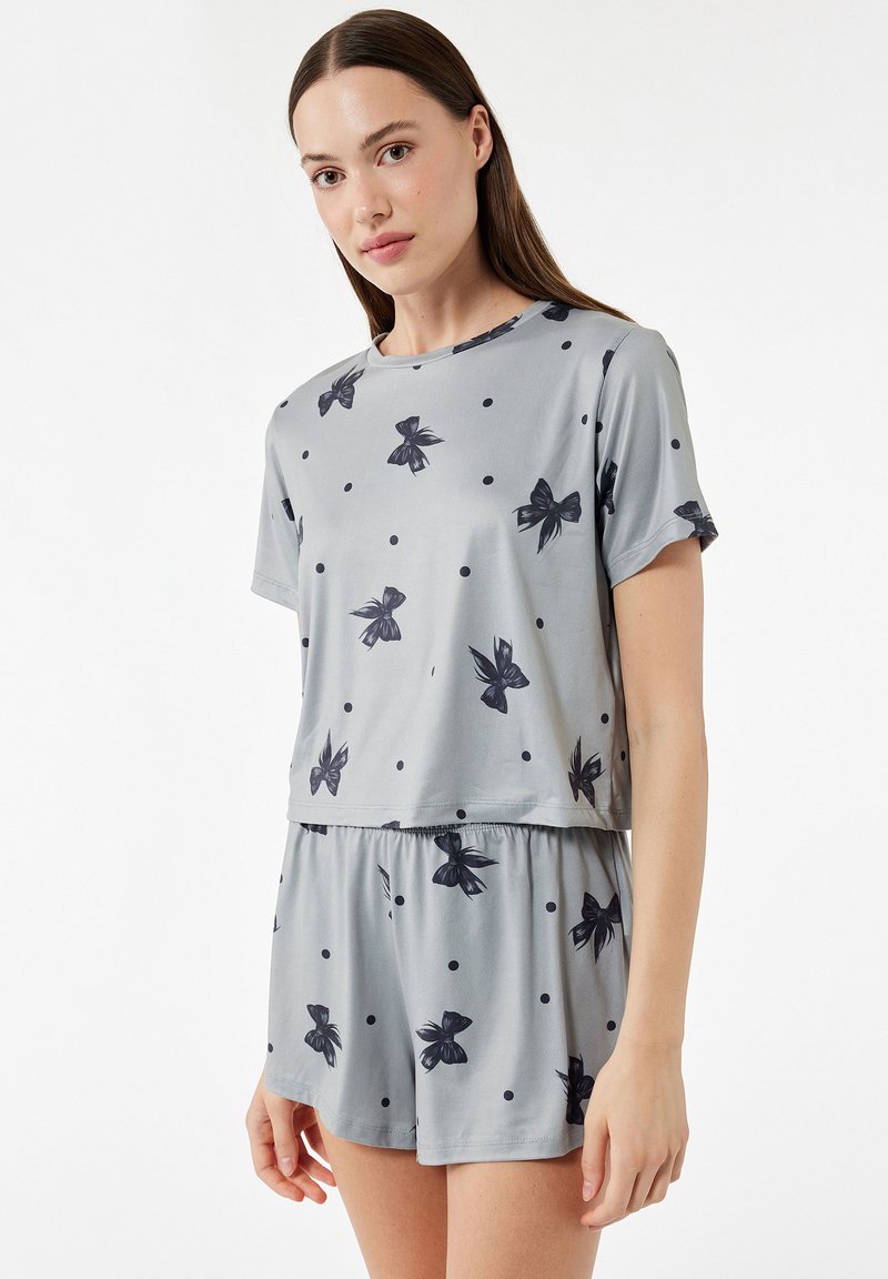Grå pyjamassæt med korte ærmer, prydet med sorte sløjfer og polka dots, lavet af et glat stof med en elastisk talje på bukserne.