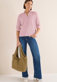 Top de manga larga texturizado en rosa claro, con cuello y escote en V, combinado con jeans acampanados azules y un bolso acolchado de un verde oliva claro.