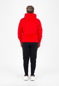 Czerwona bluza z kapturem, długimi rękawami i ściągaczami, w połączeniu z czarnymi spodniami dresowymi i białymi trampkami. Prosty design, bez widocznych logo.