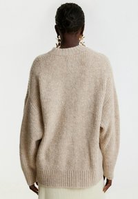 Maglione beige oversize in maglia con texture a coste e spalle scese. Maniche lunghe e scollatura a girocollo. Tessuto morbido e caldo.