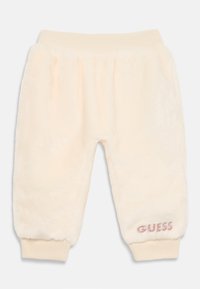 Vauvan vaaleankreemi pehmeät housut, joissa on ribbivartalo ja -hihansuut, ja vasemmassa nilkassa pieni vaaleanpunainen "GUESS" -logo.