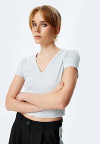 Grå cropped t-shirt i ribbet stof med V-udskæring og korte ærmer; parret med højtaljede sorte bukser med knapdetalje.