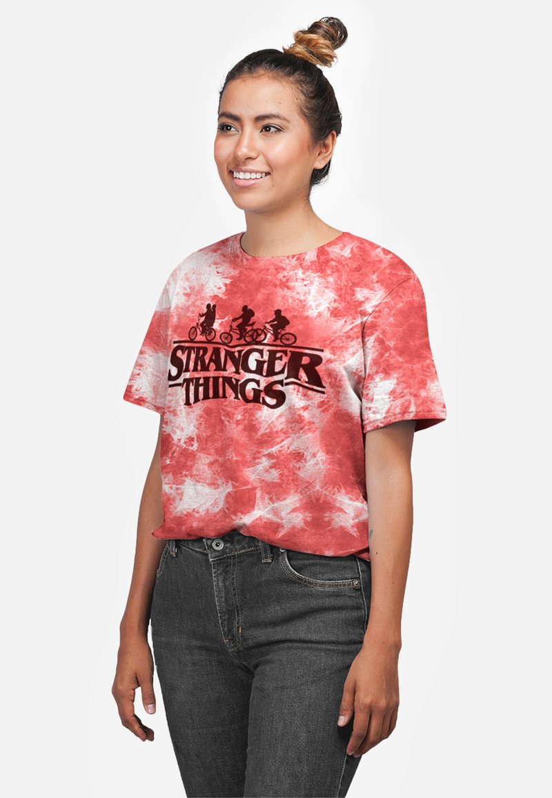 Rød og hvid tie-dye kortærmet t-shirt med "STRANGER THINGS" logo i sort, med en silhuetgrafik af karakterer på cykler.