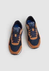 Zapatillas de malla en color navy con acentos de ante marrón; cuentan con cordones en la parte frontal, cuello acolchado y una mediasuela blanca en contraste. Etiqueta del logo en la lengüeta.