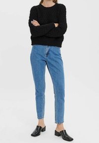 Schwarzer Strickpullover mit strukturiertem Muster, kombiniert mit hellblauen, hochgeschnittenen Jeans und schwarzen Blockabsatz-Mules.