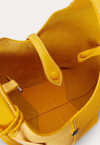 Indersiden af en gul lædertaske med struktureret foret, en strop med trykknap og en metalbeslag på siden til lukning.