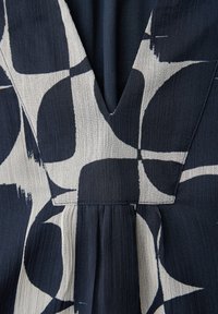 Gros plan sur un tissu de robe bleu foncé et blanc avec un motif géométrique abstrait et arrondi, et un détail d'encolure en V profond.
