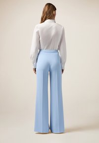 Lichtblauwe uitlopende broeken met een gladde textuur, hoge tailleband en zijschoenen; gecombineerd met een frisse witte blouse met lange mouwen.