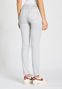 Jeans ajustados gris claro con bolsillos traseros, que presentan una textura de denim suave y una cinturilla alta. Combinados con zapatillas blancas.