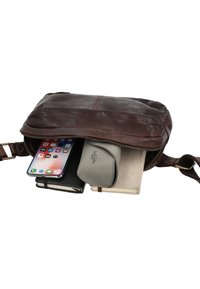 Sac bandoulière en cuir marron partiellement ouvert montrant à l'intérieur un smartphone, un carnet noir, une pochette grise et un portefeuille beige.