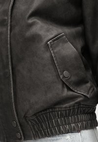 Czarna skórzana kurtka z fakturowym wykończeniem, kieszenią na zatrzask oraz elastycznym paskiem w talii dla dopasowanego kroju.