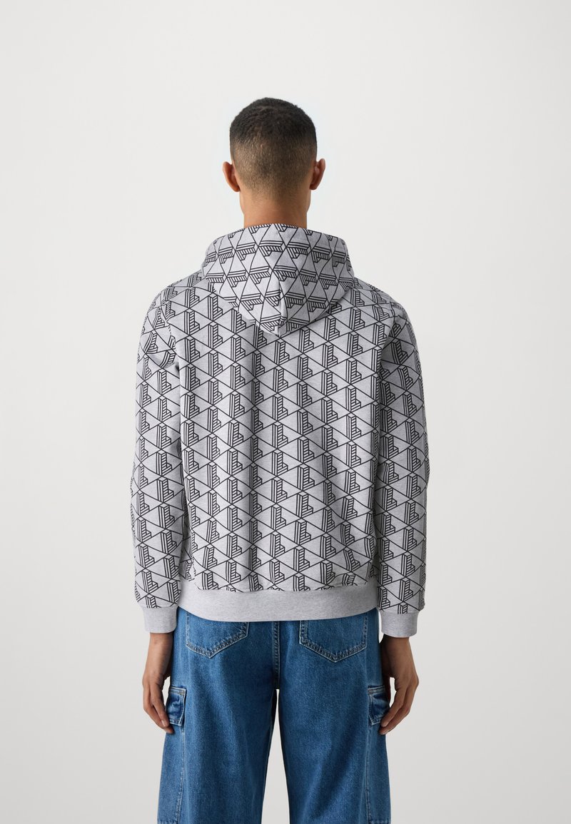 Grauer Kapuzenpullover mit schwarzem geometrischem Muster. Verfügt über eine sanft strukturierte Oberfläche und einen gerippten Saum. Kombiniert mit blauen Cargo-Hosen.