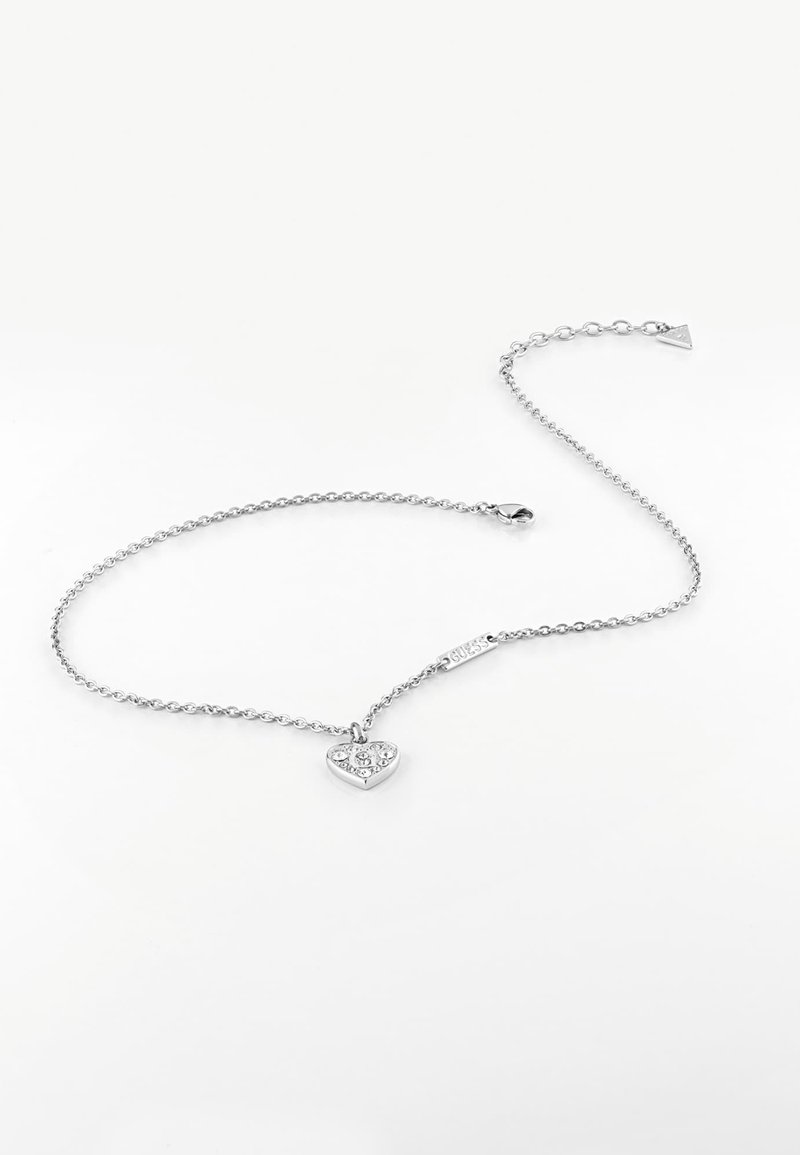 Collier chaîne en argent avec un pendentif cœur orné de petits cristaux et un fermoir, posé à plat sur un fond blanc.
