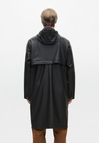 Cappotto impermeabile nero con cappuccio, caratterizzato da un design lungo e ampio e un retro a strati. Realizzato in materiale liscio e lucido con chiusure a scatto.