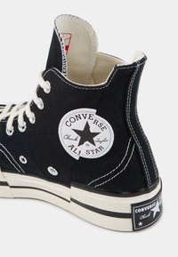 Baskets montantes noires Converse Chuck Taylor All Star avec lacets blancs, coutures blanches et patch logo à la cheville et au talon.