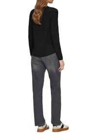 Zwarte lange mouwen top gecombineerd met grijze jeans en witte sneakers met een tan kleurige zool. De jeans hebben een vervaagde textuur en zichtbare stikdetails.