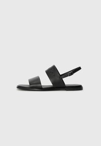 Mustad mustadest nahast sandaalid, millel on kaks laia rihma ja reguleeritav pahkluu rihm. Lame tallaga, millel on minimalistlik disain ja diskreetne brändi detail.
