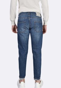 Jeans di denim blu con vestibilità affusolata, caratterizzati da due tasche posteriori, risvolti arrotolati e una finitura chiara. Indossati con sneakers bianche.