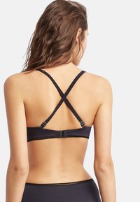 Crni bralet s ukriženim trakama, kopčanjem na kukicu, glatkom teksturom i čipkastim rubom duž trake, koji prikazuje minimalistički dizajn.