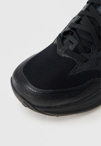 Μαύρο αθλητικό παπούτσι με άνω μέρος από δίχτυ, υφασμένη μύτη και ενισχυμένο σύστημα κορδονιών. Ελαστική σόλα με διακριτικές σχεδιαστικές πινελιές.