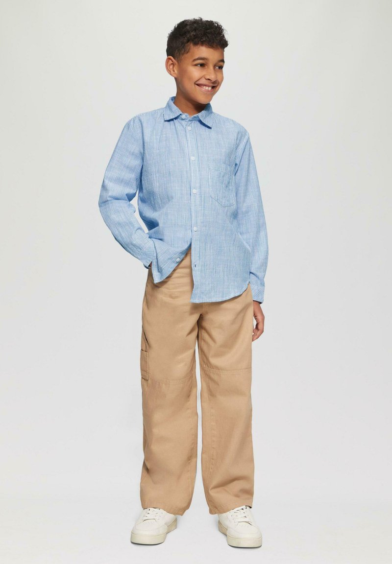 Blauw en wit gestreept overhemd met lange mouwen, met knopen, voorzien van een borstzak, gecombineerd met beige cargobroek en witte sneakers.