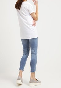 Bílá bavlněná trička s krátkým rukávem, kombinovaná s světle modrými skinny džíny a šedými slip-on botami s bílou platformou.