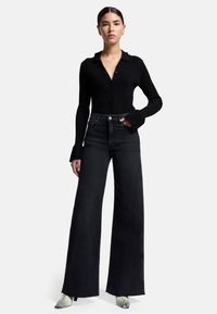 Camicia a maniche lunghe nera a coste con bottoni abbinata a jeans scuri a vita alta e gamba larga. Scarpe con una texture a motivo rettile.