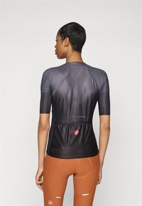 Korte ermet sykkelskjorte i mørk grå med teksturert overflate, med baklomme og røde logo-detaljer; kombinert med brune sykkelshorts.