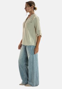 Camisa beige ligera de manga larga con cuello con muesca y bolsillo frontal, combinada con vaqueros anchos de pierna en azul claro hechos de denim.