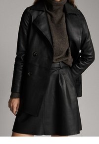 Sort læder dobbeltradet jakke med brede reverser, parret med en mørkebrun turtleneck og en matchende læderskirt. Glat tekstur.