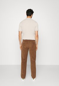 Beige ribbad kortärmad skjorta, bruna kordflätenbyxor och vita sneakers med gröna detaljer, sedd bakifrån.