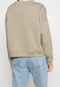 Sweat-shirt beige surdimensionné avec un col rond et des poignets côtelés, associé à un jean bleu clair taille haute. La texture douce du tissu est visible.