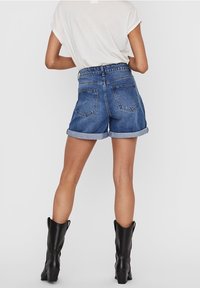 Shorts de mezclilla de tiro alto con dobladillos enrollados, que cuentan con dos bolsillos traseros, combinados con una camiseta blanca holgada y botas negras hasta la rodilla.