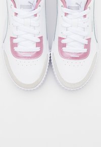 Une paire de baskets Puma blanches avec des accents roses, des lacets blancs et des embouts en daim gris clair, vue de dessus sur un fond blanc.