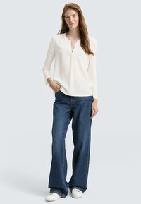 White long-sleeve blouse with a V-neck and a relaxed fit, paired with dark blue wide-leg jeans and white sneakers. Plain textures, no patterns.