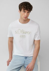 Weißes Baumwoll-T-Shirt mit Rundhalsausschnitt, das geprägten Text "s.Oliver ELEVATED ESSENTIALS SINCE 1969" in Gold und Grau zeigt.