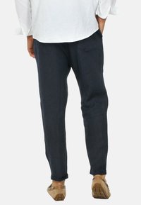 Pantaloni in lino blu scuro da uomo con una vestibilità rilassata, caratterizzati da un design a gamba affusolata e con risvolti, abbinati a scarpe chiare.