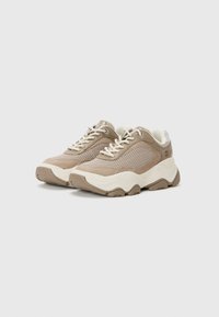 Sneaker beige con tomaia in mesh e suede, suola in gomma crema, punta rotonda e lacci a contrasto. Presenta una collare imbottito e un design testurizzato.