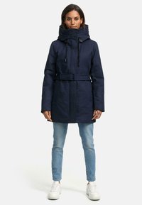 Manteau long bleu marine avec un col haut, des cordons de serrage ajustables et une taille ceinturée. Présente des poches à boutons et une texture lisse.