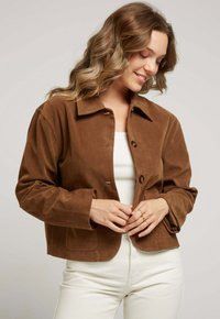 Veste courte en daim marron avec un col, fermeture à boutons et poches latérales. Texture lisse, coupe décontractée et manches longues.