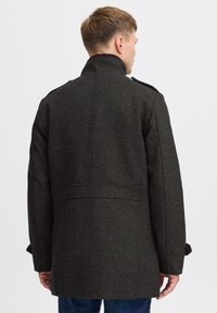 Abrigo de mezcla de lana oscura con un patrón de espiga, cuello alto y hombreras, que presenta un corte entallado y un detalle de costura en la parte posterior.