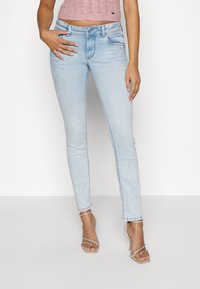 Světle modré skinny džíny vyrobené z denimu s klasickým pětikapsovým designem, jemným vyblednutím a mírným poškozením na manžetách.