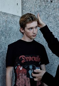 Svart T-shirt med en grafisk design av Dracula med röda och vita accenter. Modellen har medellångt hår och en synlig näsring.