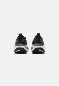 Baskets de sport noires avec un dessus lisse, des accents texturés, un col rembourré et une semelle blanche avec des détails en motif et un logo.