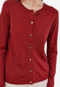 Cardigan rosso lavorato a maglia con scollatura tonda, chiusura frontale con bottoni e maniche lunghe. Presenta bottoni in metallo e una texture morbida.