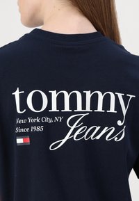 Námorně modré bavlněné tričko s bílým nápisem "tommy Jeans", s textem "New York City, NY Since 1985" a malou vlajkovou emblematickou značkou.