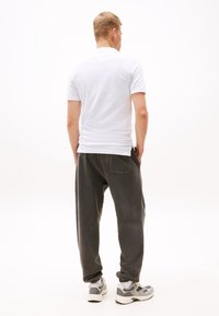 Vit kortärmad t-shirt och mörkgrå löst sittande sweatpants med sidofickor, i kombination med grå och vita sportskor.