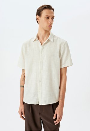 Camisa de botones de manga corta en beige claro, hecha de un tejido texturizado. Presenta un cuello puntiagudo y un corte relajado.